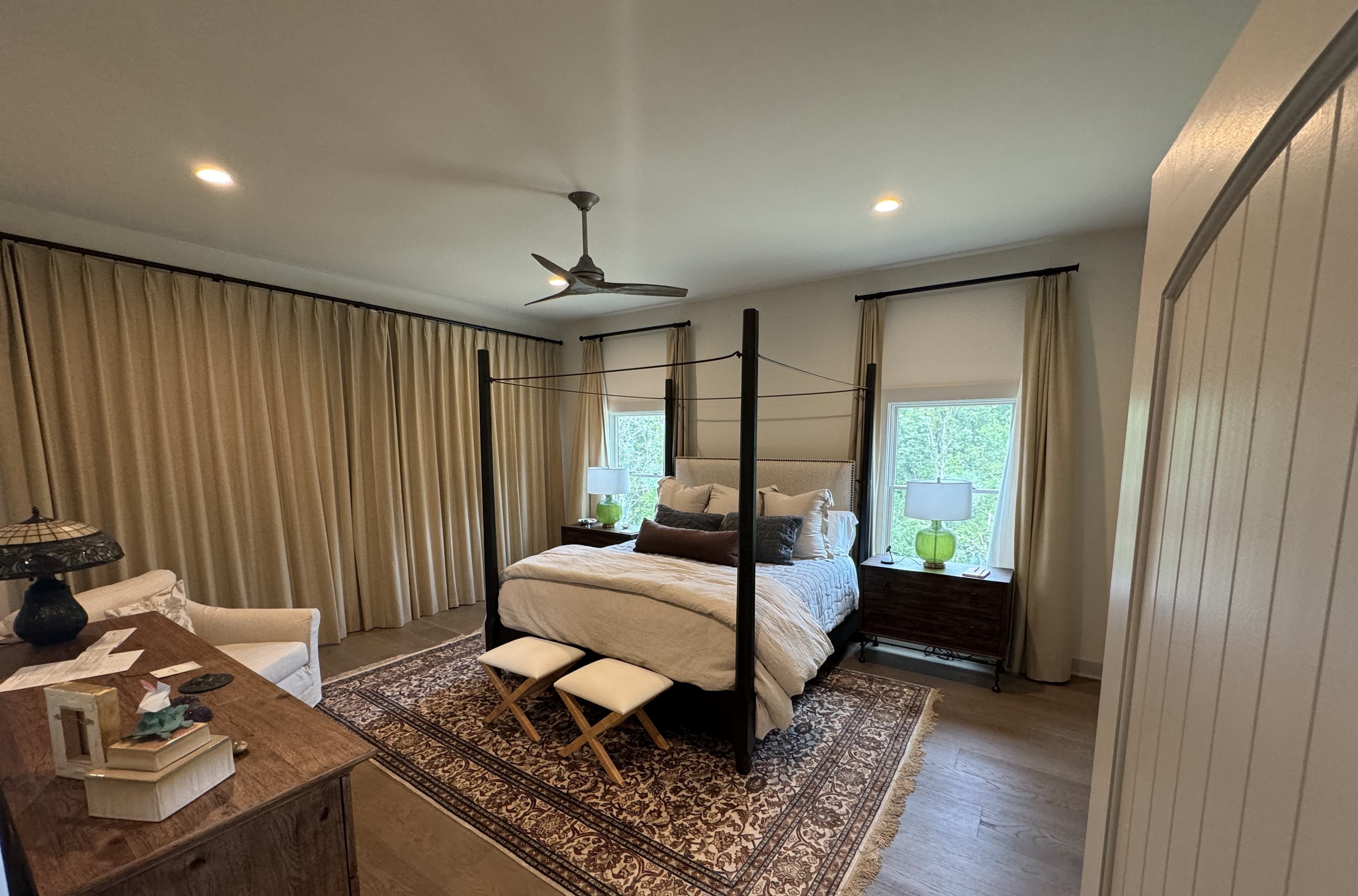 Finished primary bedroom with a four-poster bed, hardwood floors, and tall draped windows