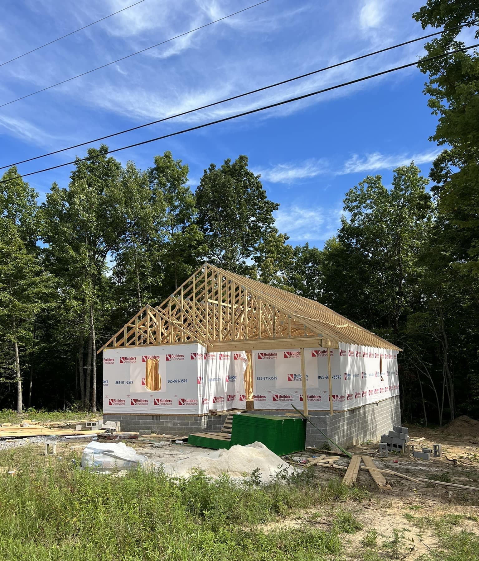 House framing with roof trusses on a block foundation, set on a wooded lot during an S&T Construction build