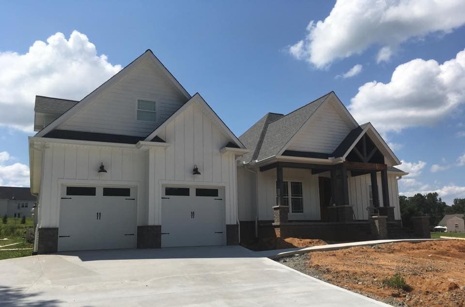 White custom home with board-and-batten gables and a covered porch, sitting on a lot that is still being finished, built by S&T Construction